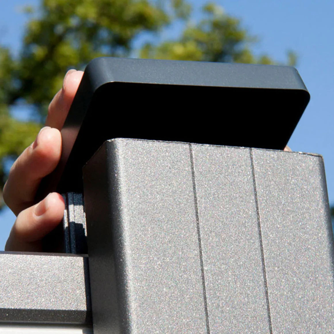 Hand installing black aluminum fence post cap on square metal fence post for a clean, weather-resistant outdoor fence finish