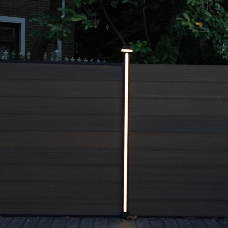 Vertical LED fence post light illuminating composite fence at night