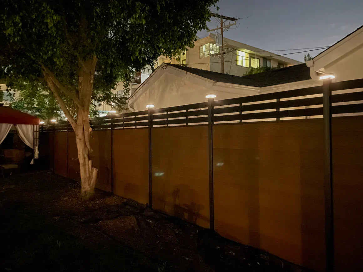 Solar LED fence post lights illuminating a modern WPC privacy fence at night